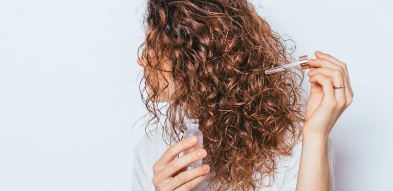 A woman putting hair serum in her hair.