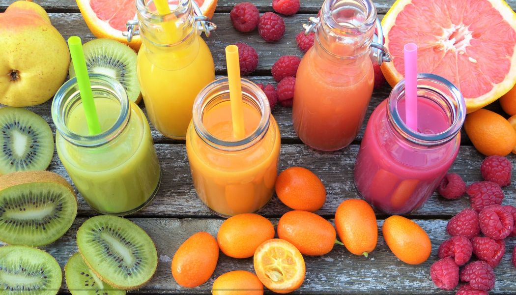 Four bottles of colorful fruit juice on a table, surrounded by different types of juice.