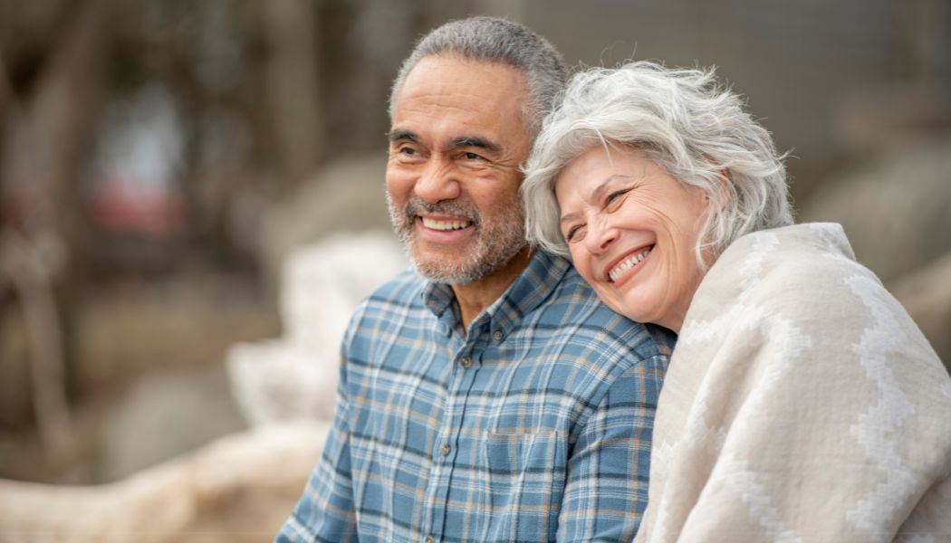 A retired couple sitting together outside, smiling.