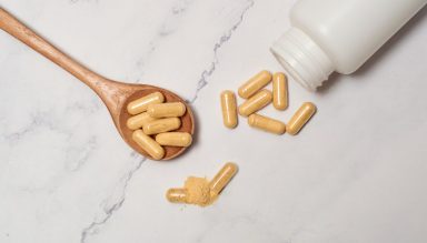 A bottle of probiotic pills spilling out onto a wooden spoon and white counter.